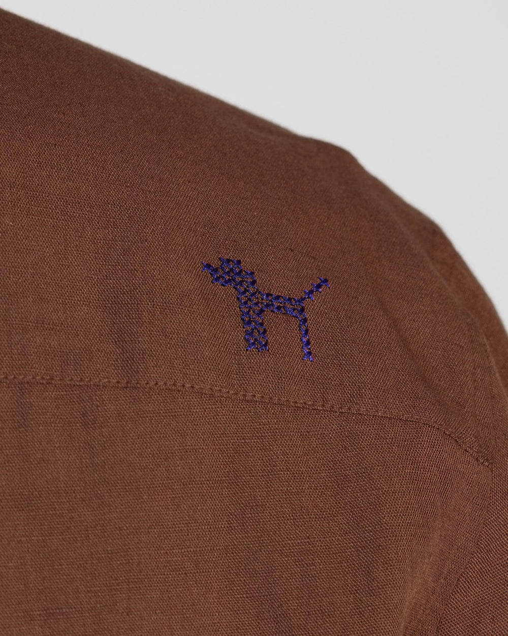 Close-up of a navy dog embroidery on a brown Classic Shirt.