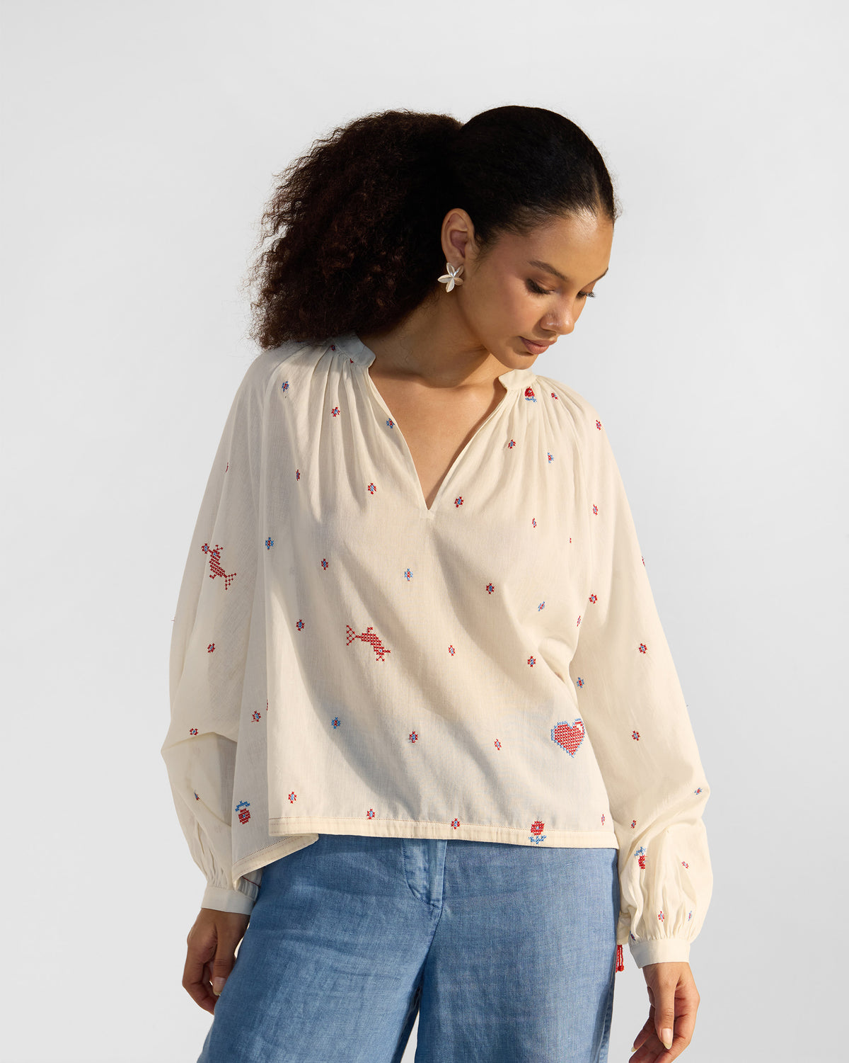 Person wearing an ivory Tahi top with red cross-stitch embroidery.