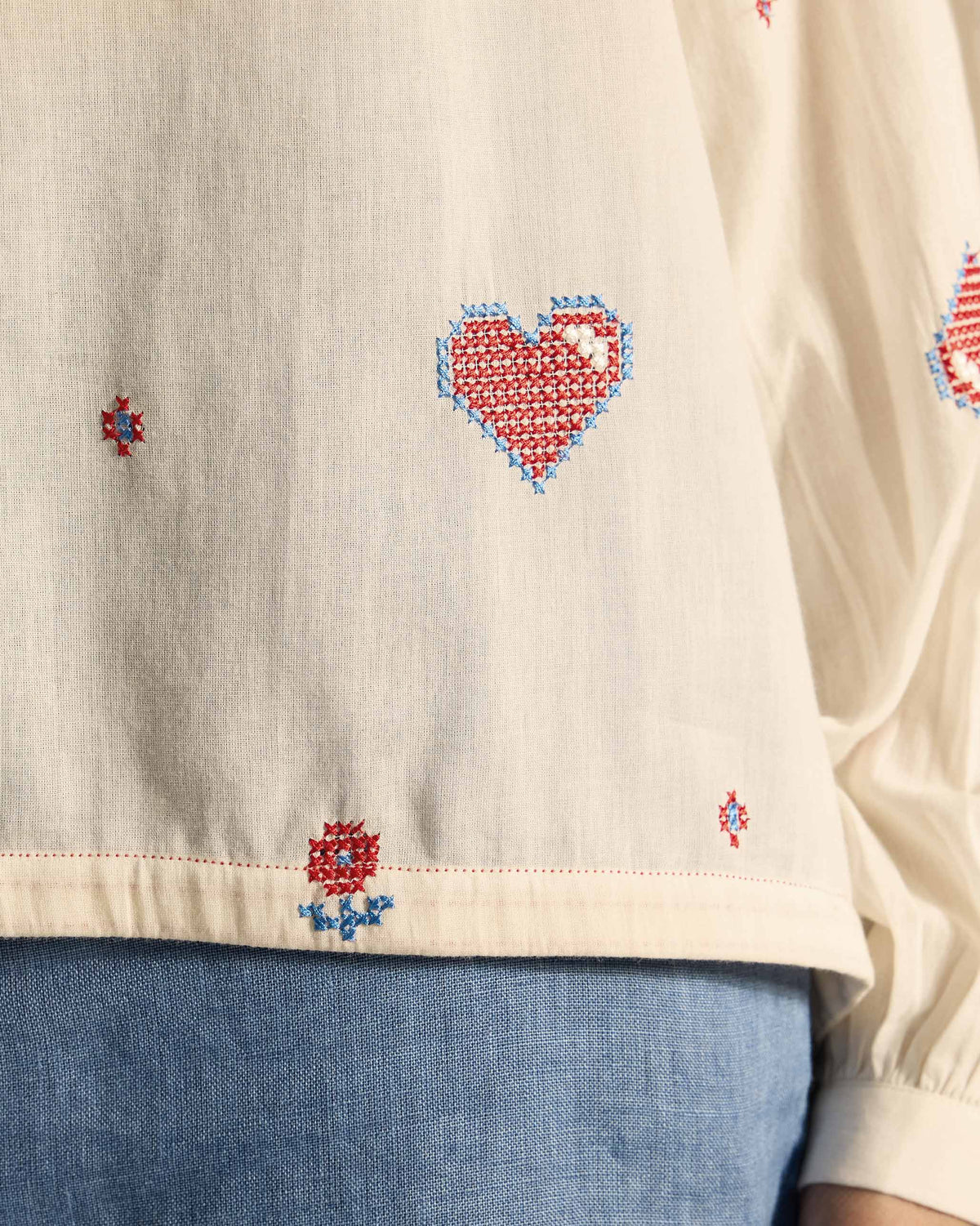 Close-up of a red heart embroidery on an ivory Tahi top.