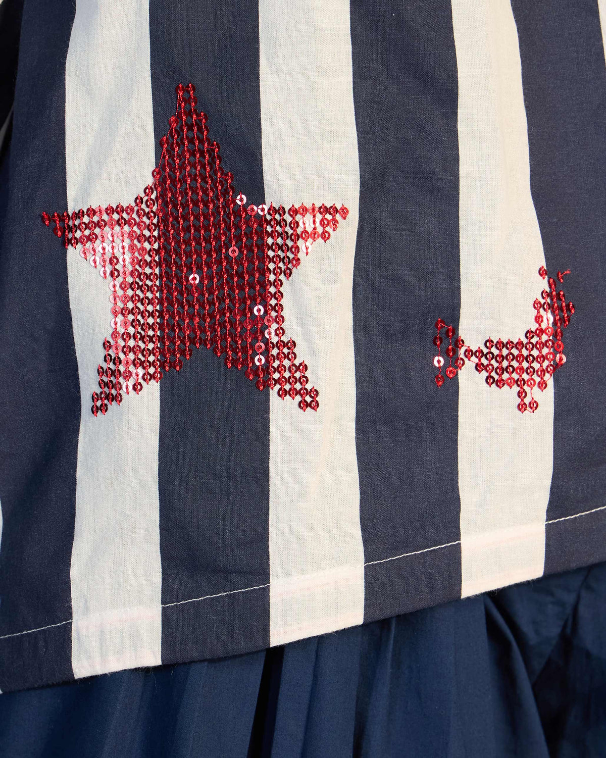 Close-up of red sequin star motifs on a navy and white striped Zaya top.