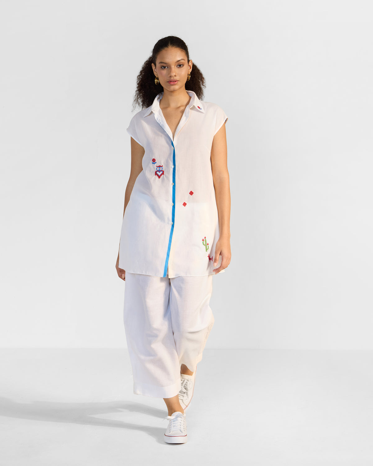 Person wearing a white Eira top with blue trim and scattered embroideries.