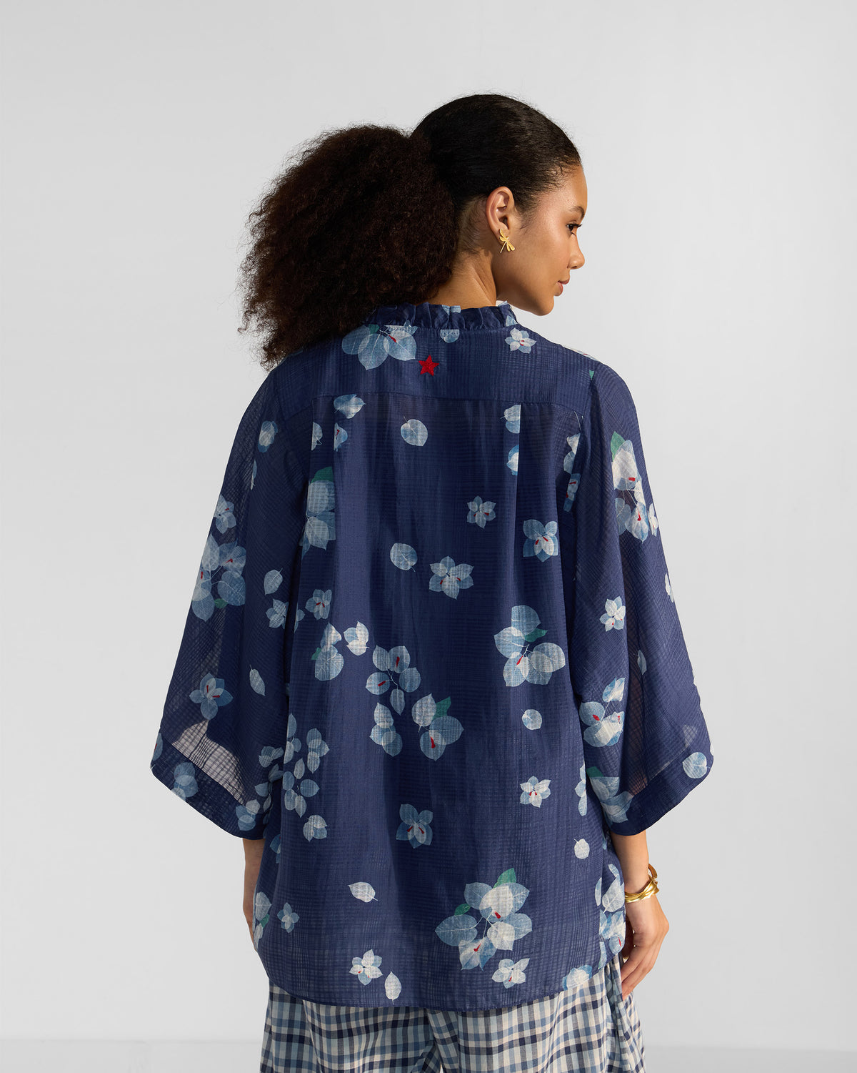 Back of a navy Lina shirt with slip showing a ruffled collar and red star embroidery.