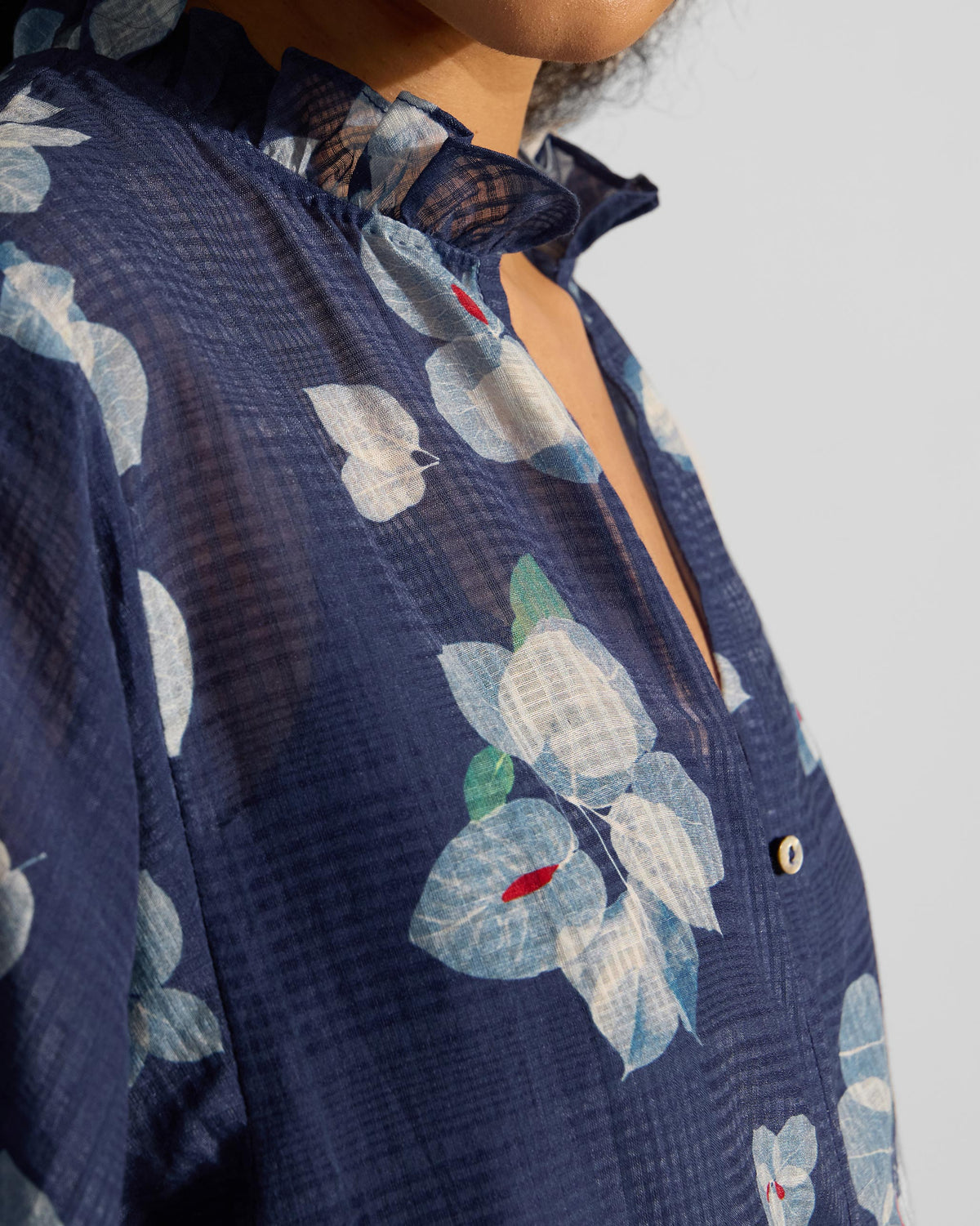 Close-up of a navy Lina shirt with slip showing the ruffled collar and bougainvillea print.