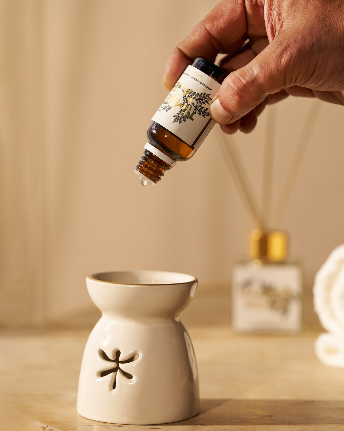 Hand tipping an amber Timbertale oil vial to drop oil into a ceramic burner.