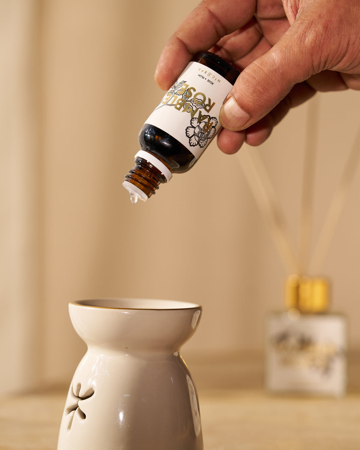 Hand dripping Ramblerose oil onto a cream ceramic oil burner.