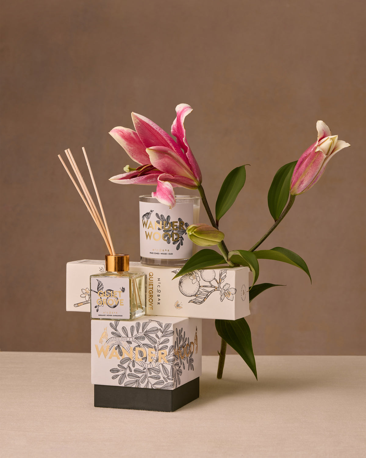 Wanderwood candle stacked with other Nicobar fragrance boxes and a diffuser.