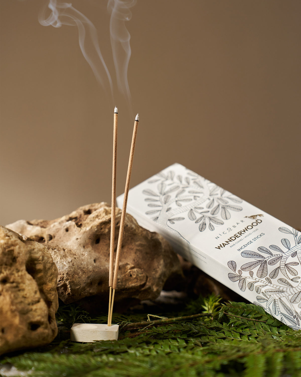 Lit Wanderwood incense sticks in a ceramic holder beside the box.