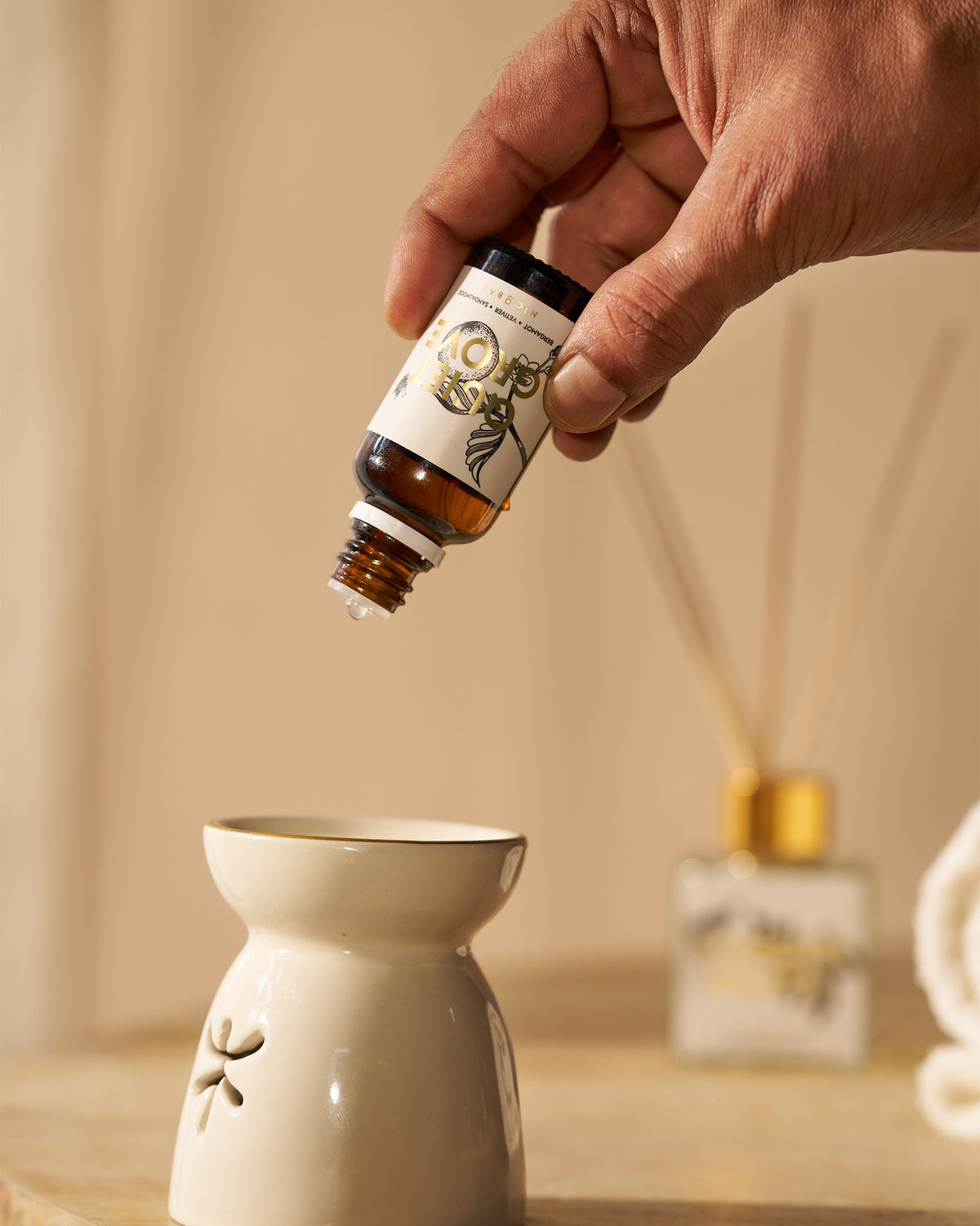 Hand dripping Quiet Grove oil onto a white ceramic oil burner.