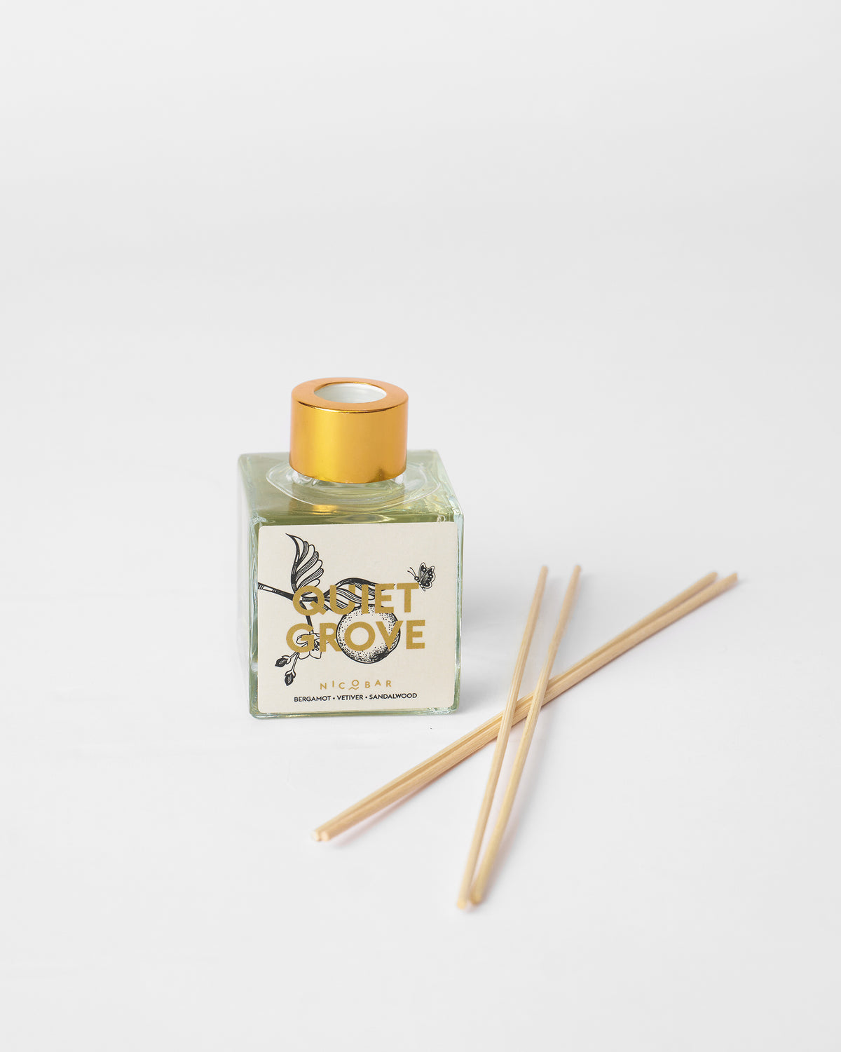 Quiet Grove diffuser bottle with wooden reeds laid beside it.
