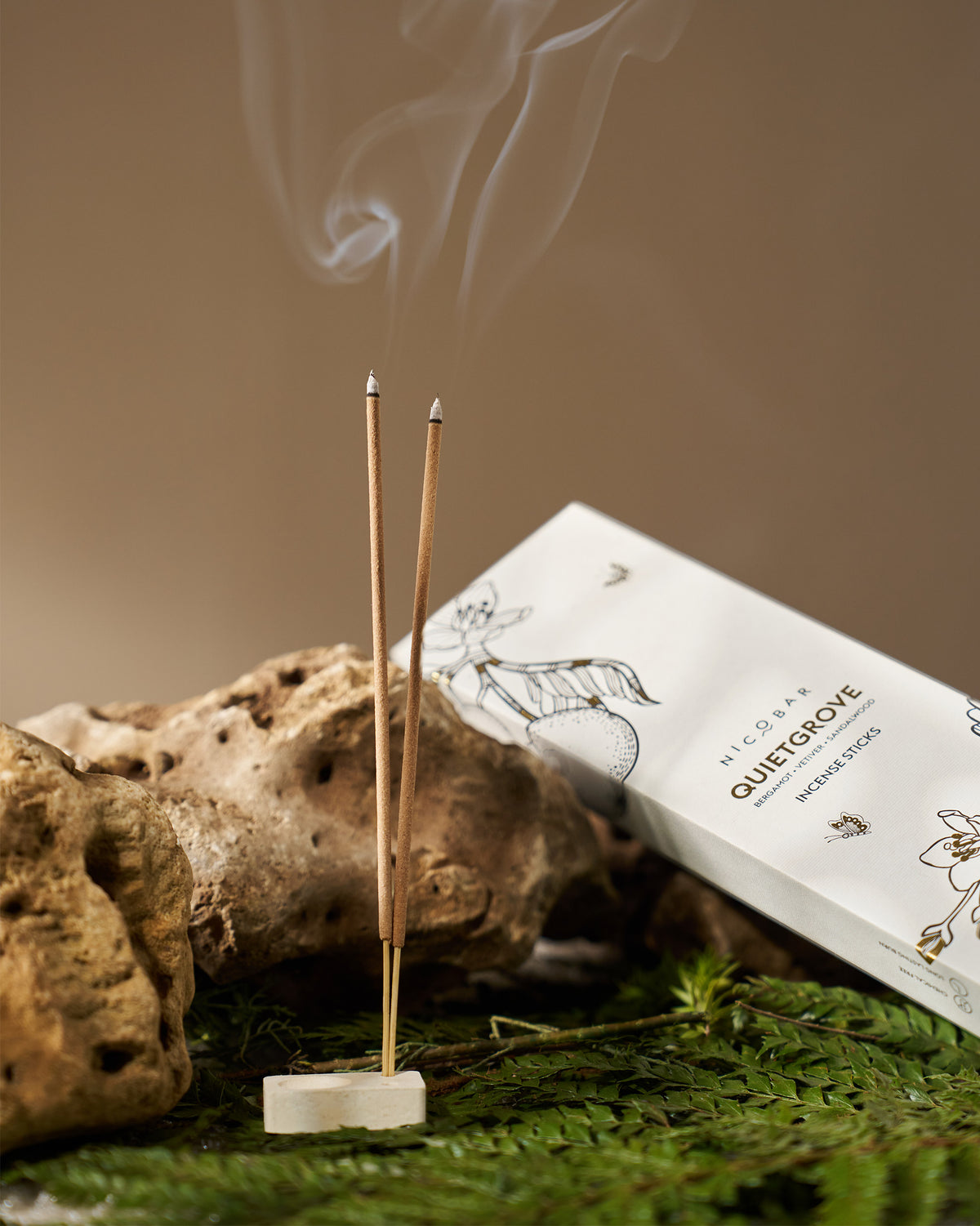 Quiet Grove Incense Sticks burning in a stone holder beside their box.