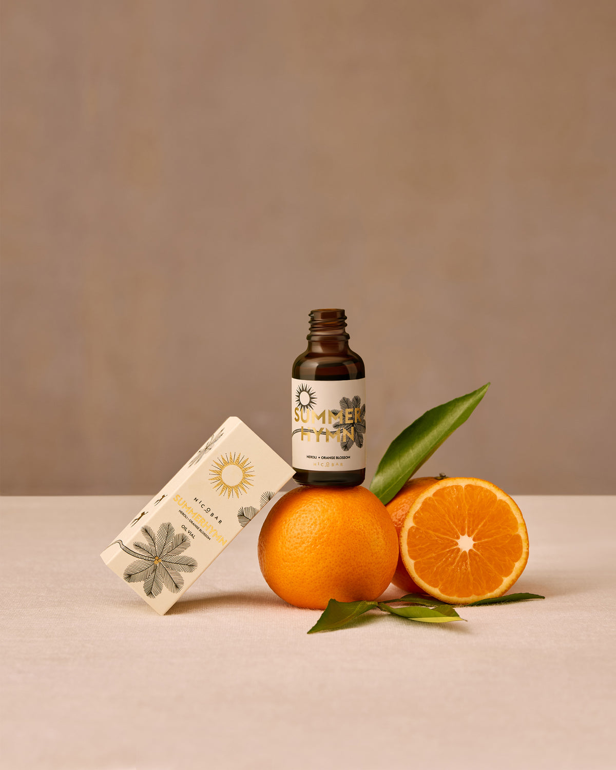Summerhymn oil vial on an orange beside its box and citrus fruit.