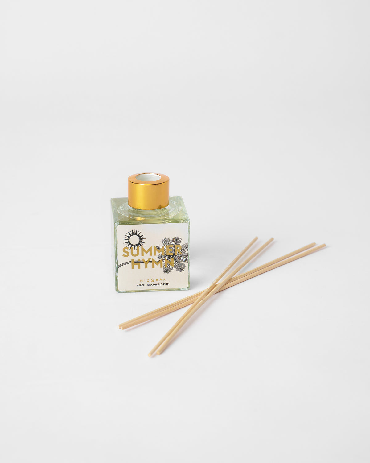 Summer Hymn glass diffuser bottle with gold cap and reeds laid beside it.