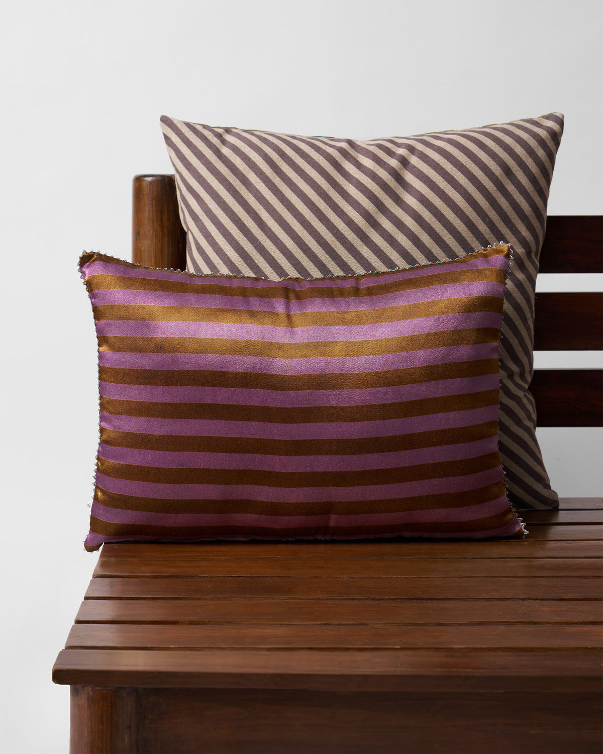 Pink and brown striped cushion in front of a brown and cream striped cushion.