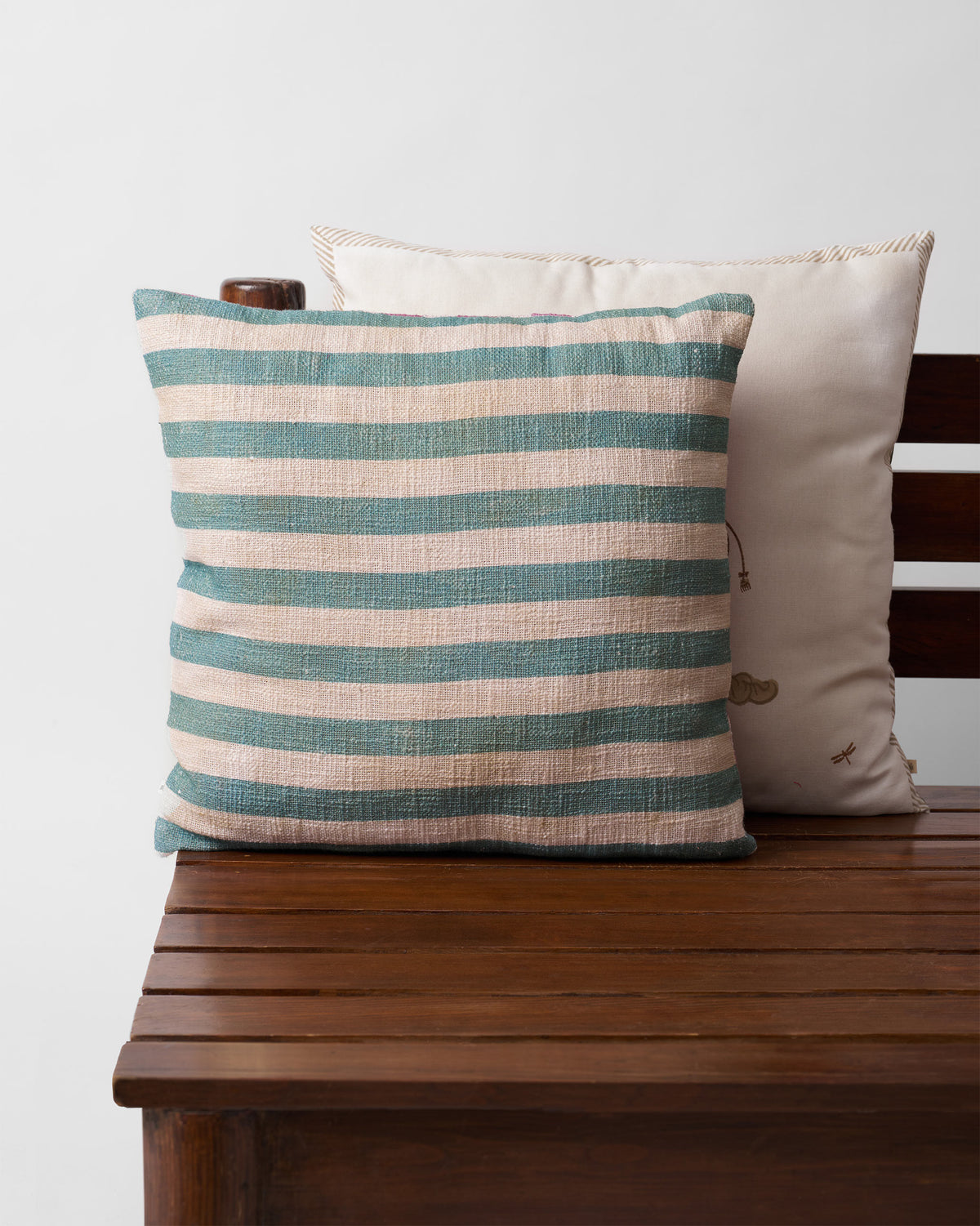 Cushion cover with teal and cream stripes on a wooden bench.