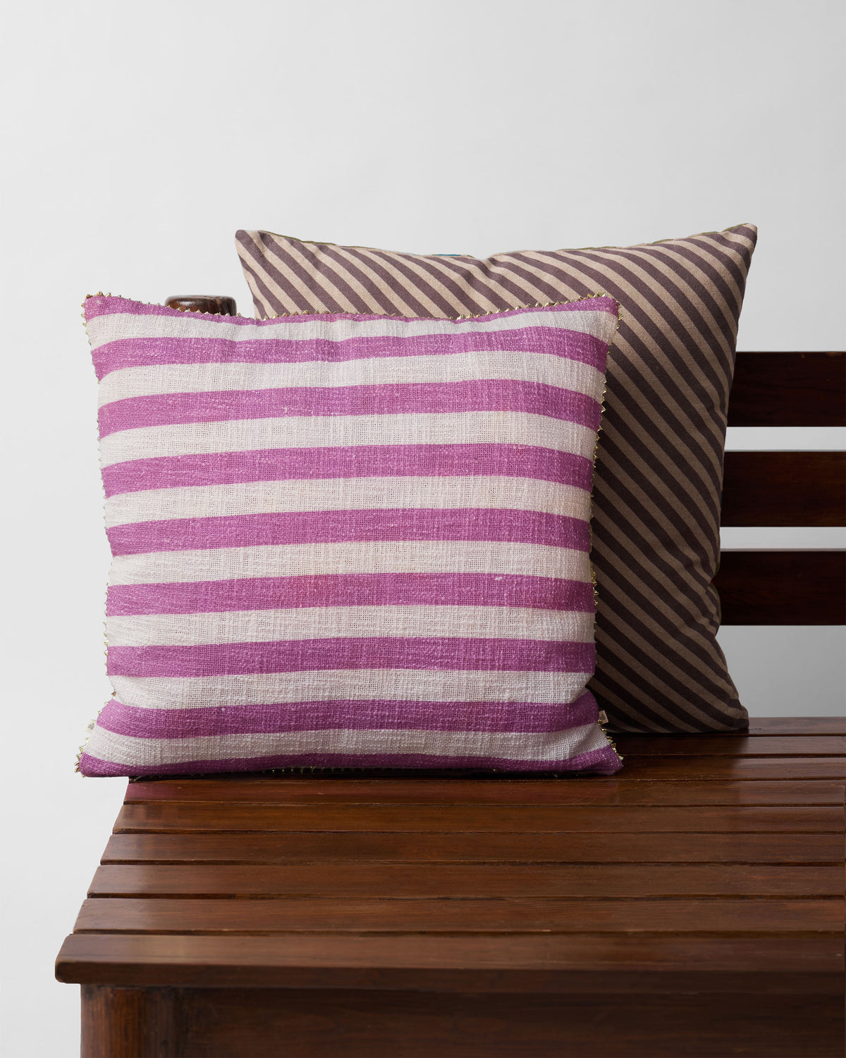 Pink and white striped Tusk Bloom Cushion Cover on a wooden bench.