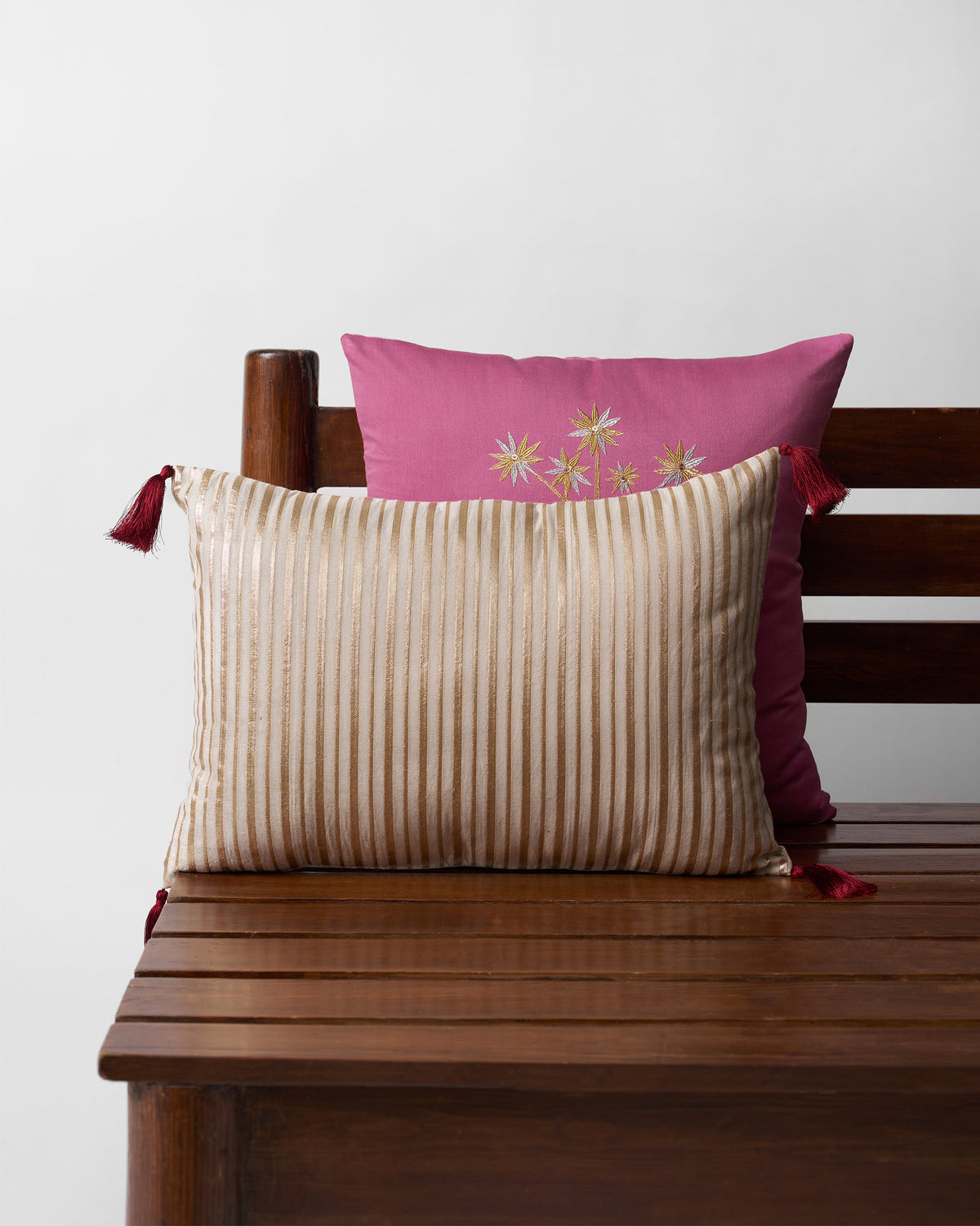 Cream cushion with gold vertical stripes and maroon tassels.