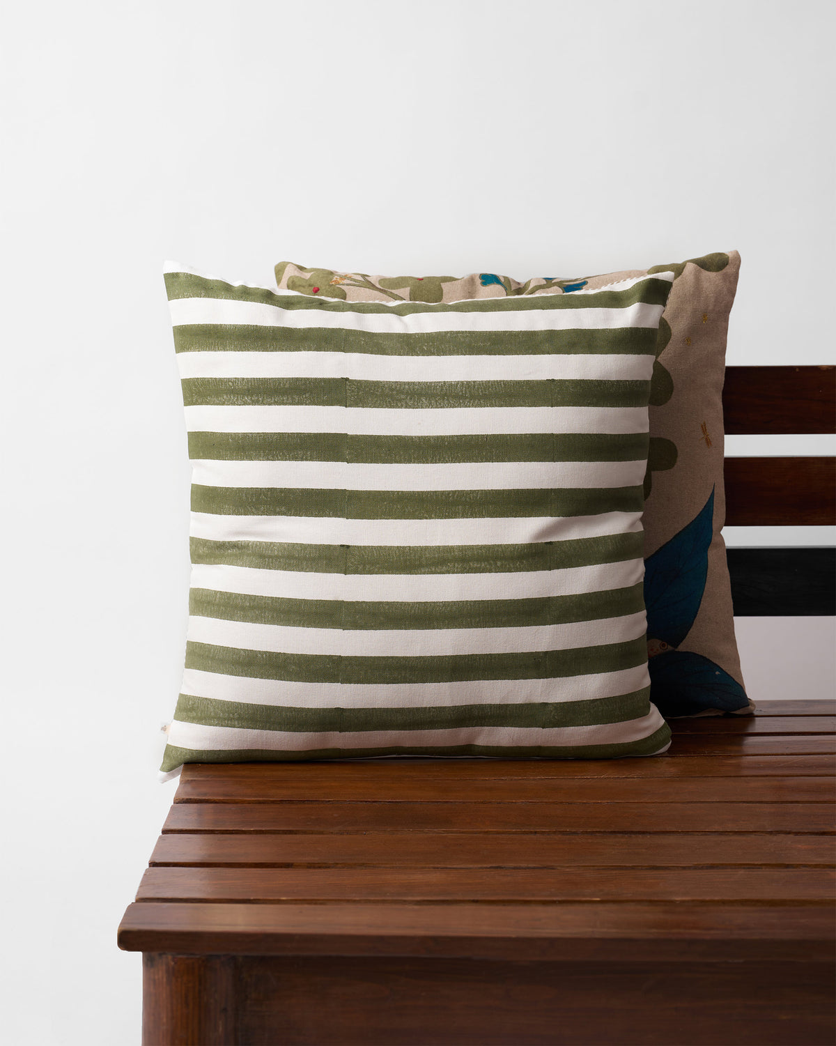 Cushion cover with olive green stripes on a cream ground, on a wooden bench.