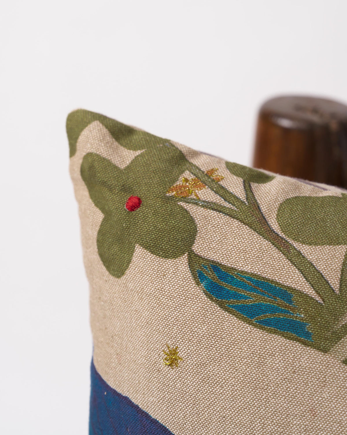 Close-up of a Fern Bloom cushion cover showing a green flower and gold leaf detail.