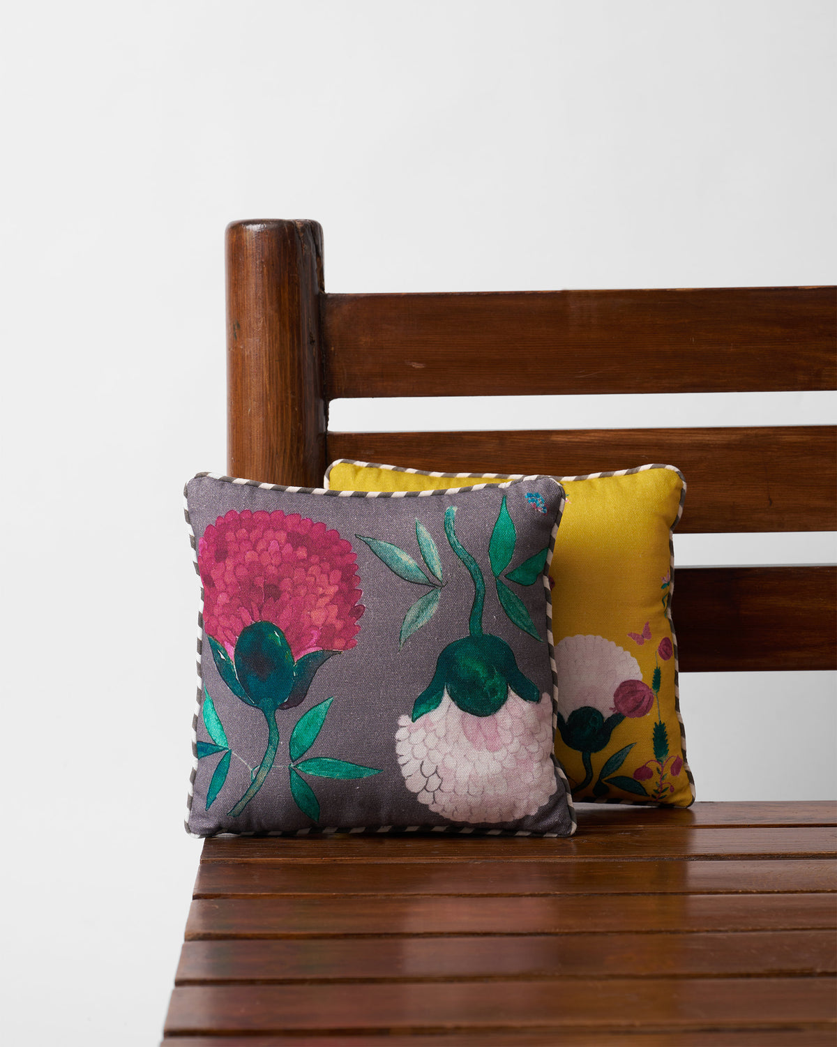 Charcoal Peony car cushion with pink blooms and striped piping on a wood bench.