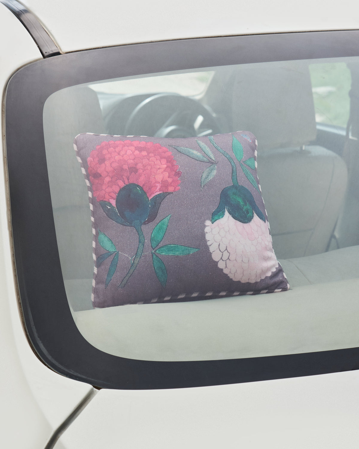 Peony car cushion with pink blooms resting on a car’s rear shelf.