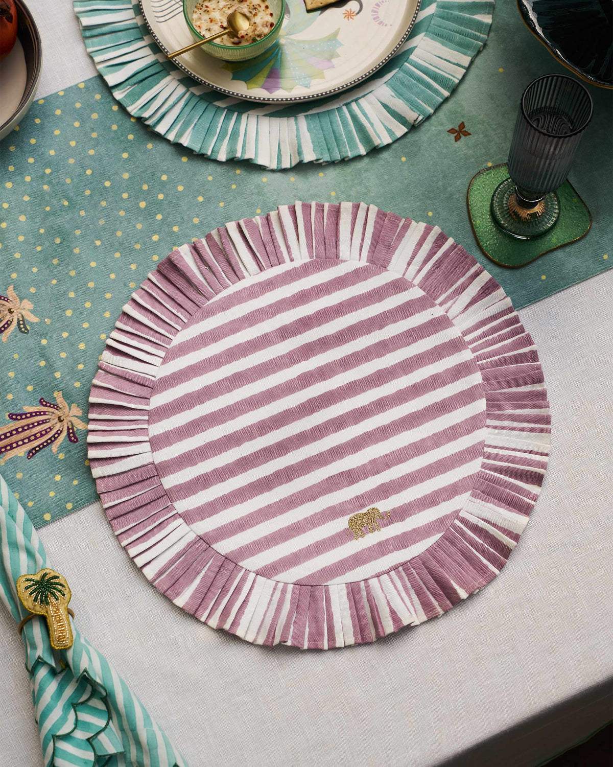 Mauve striped Yamuna placemat with a ruffled edge on a set table.