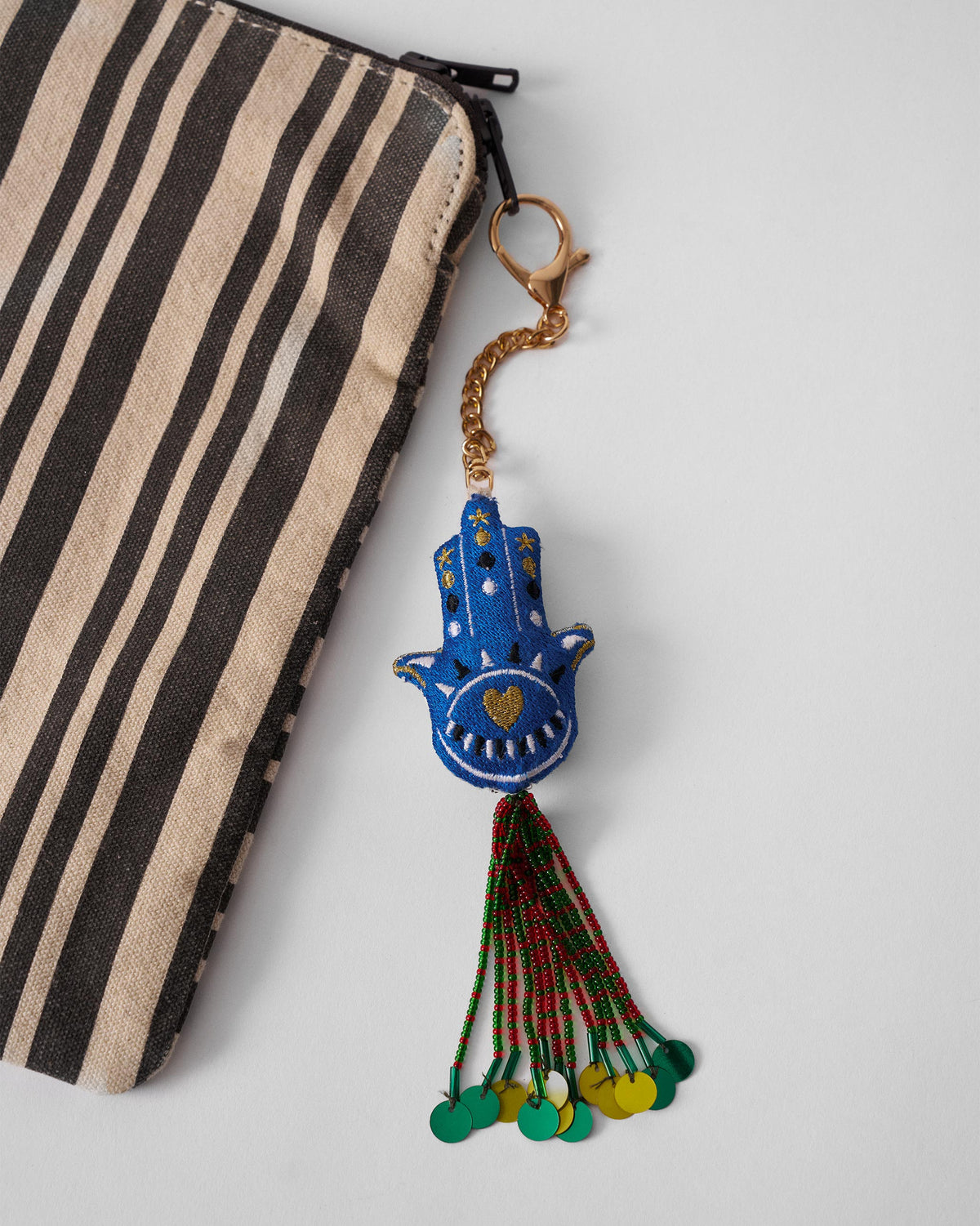 Hamsa Charm in blue with a gold heart, hanging at an angle with a beaded tassel.