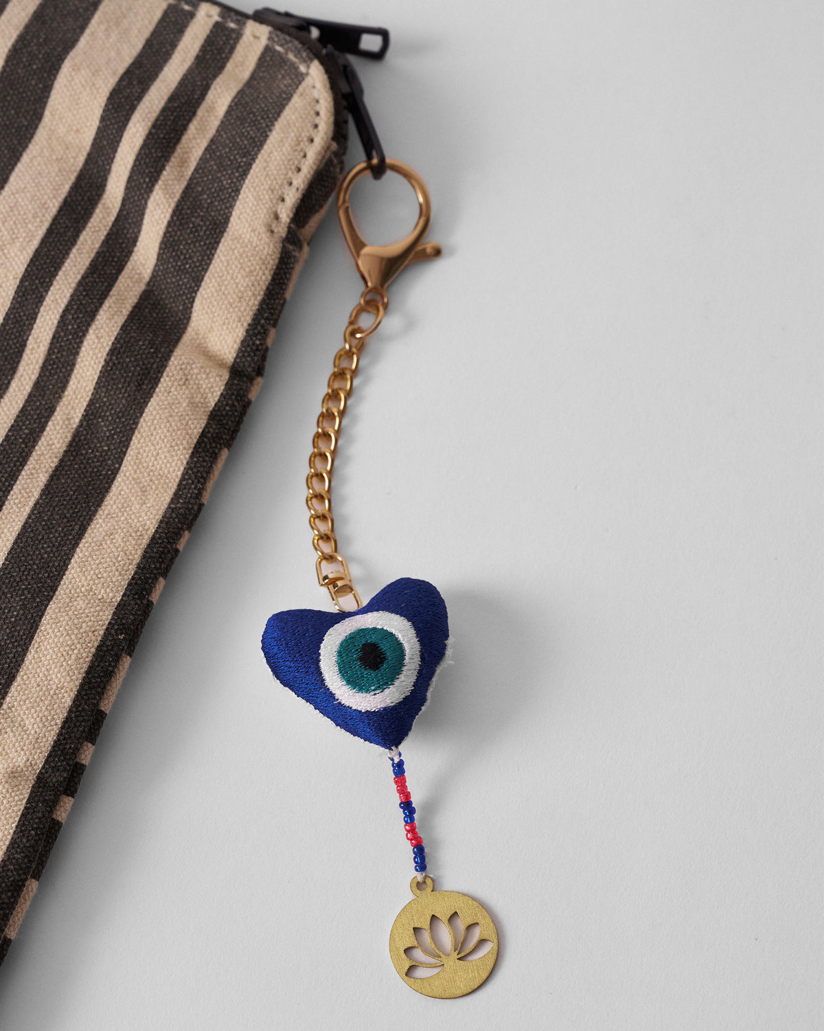 Kamal Charm with a blue heart-shaped eye motif, hanging at an angle with a gold lotus tag.