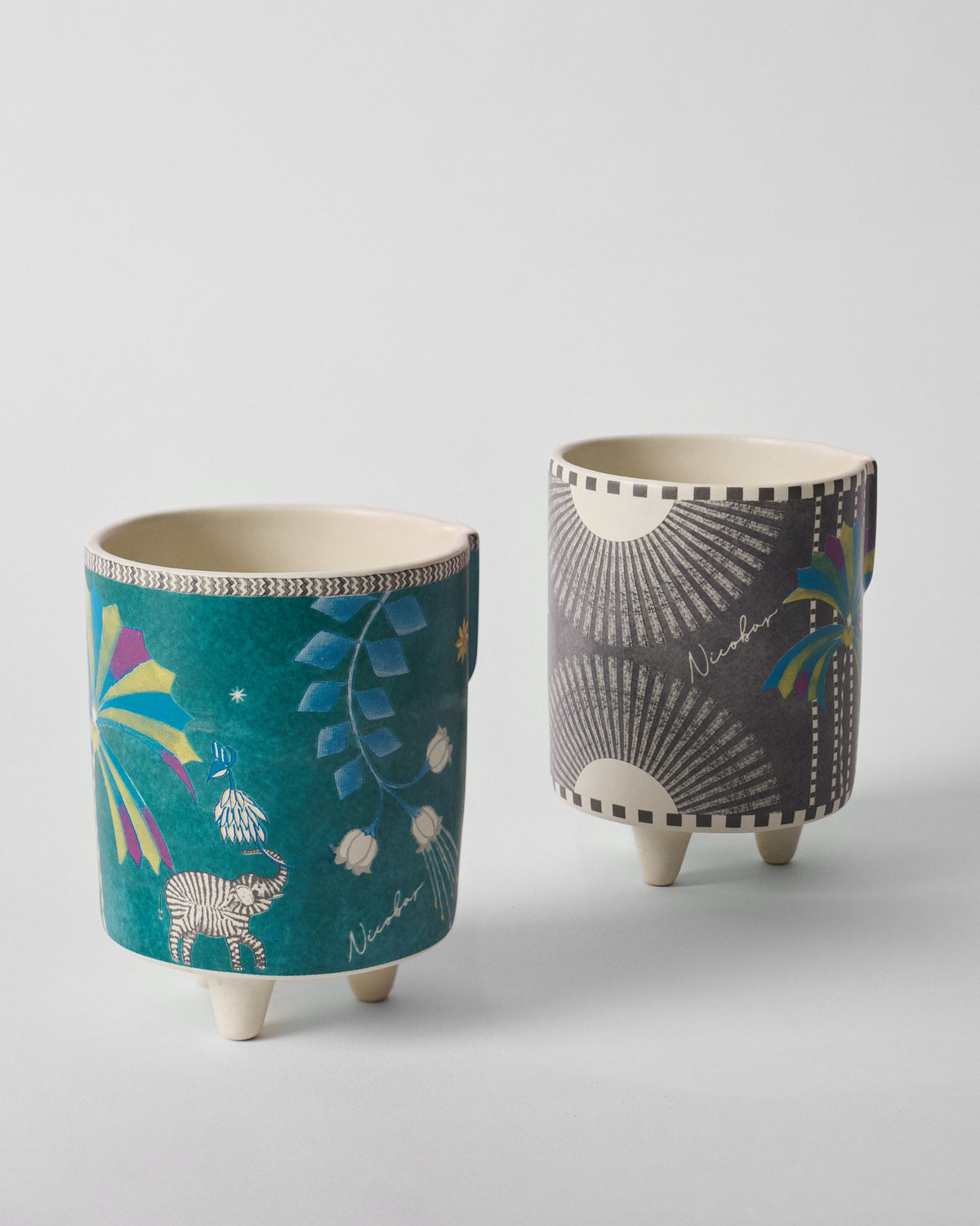 Teal and charcoal Palm Bloom planters with elephant, palm, and sunburst prints.
