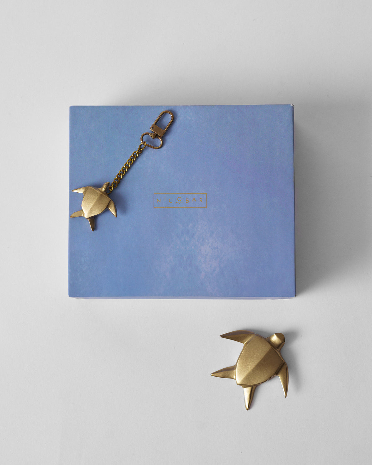 Gold turtle keychain on a Nicobar gift box with matching turtle paperweight below.