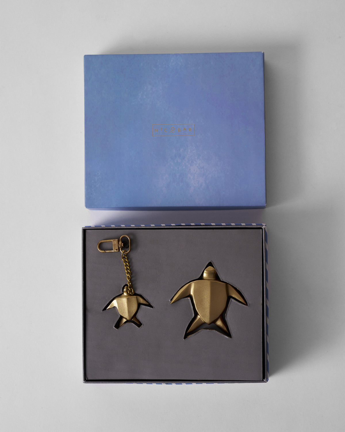 Gold turtle keychain and paperweight nested in an open Nicobar gift box.