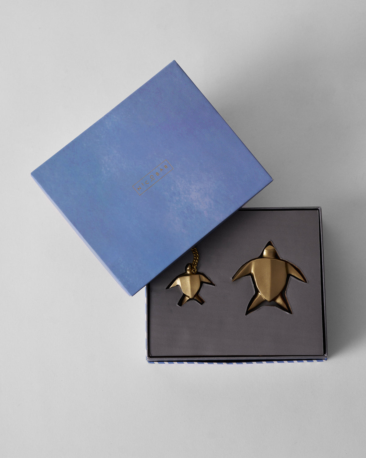 Open blue Nicobar box holding gold turtle keychain and paperweight in foam.