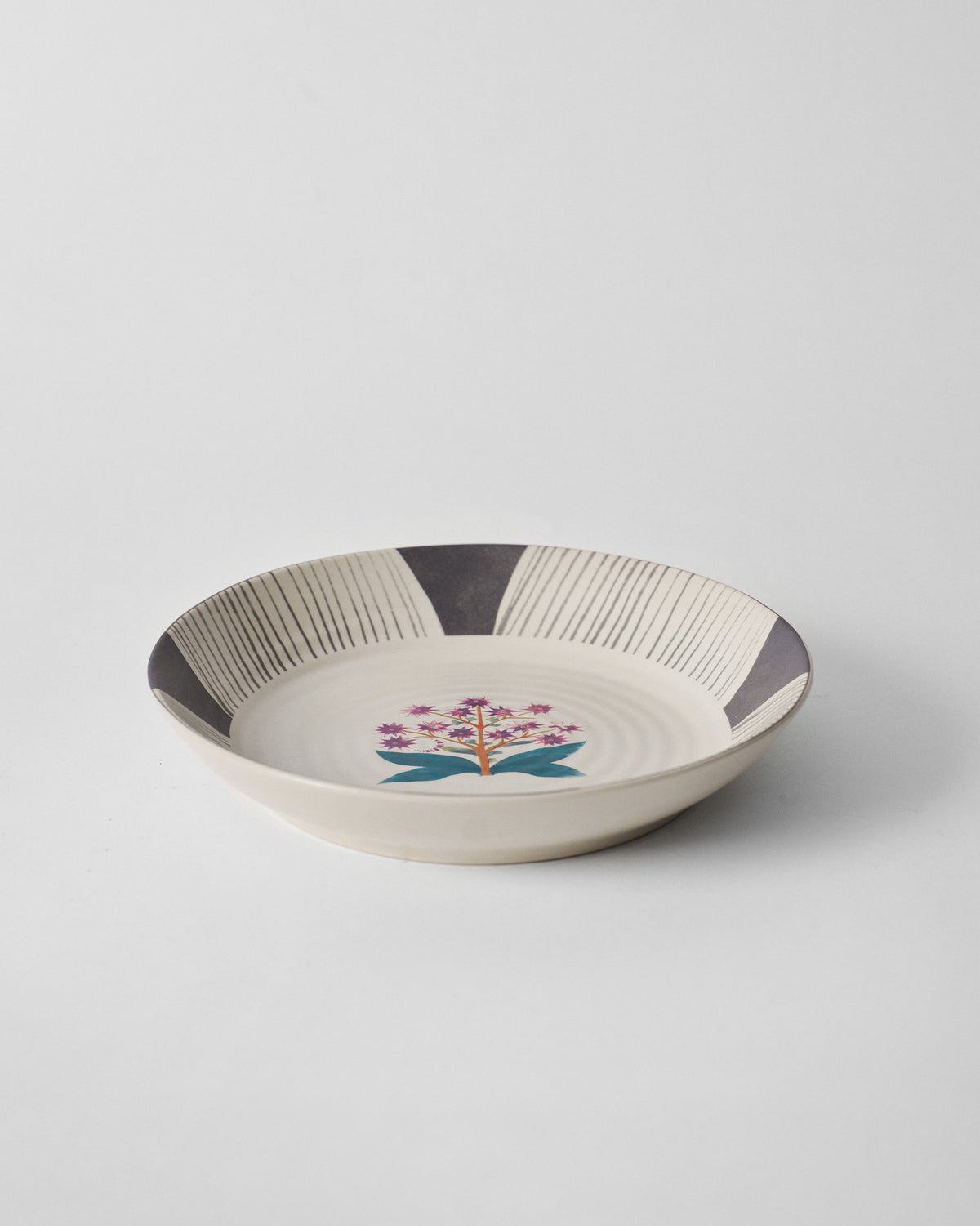 Angled view of a Mogra pasta plate with a purple flower and teal leaves.