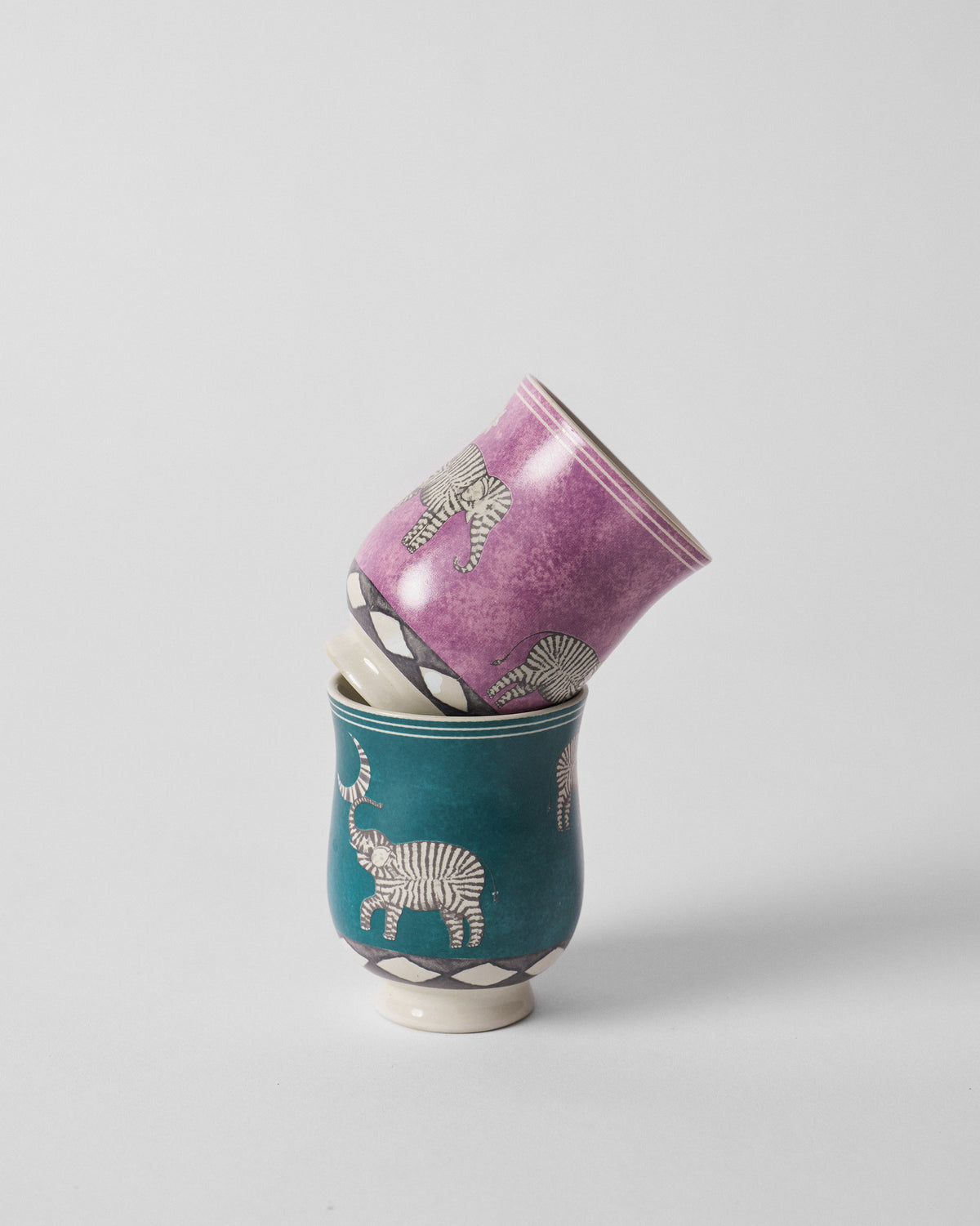 Stacked Tusk tea cups in purple and teal with elephant motifs.