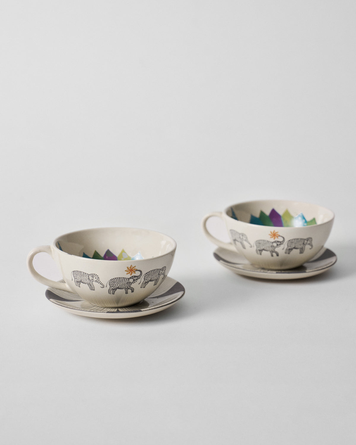 Two Palm Bloom coffee cups on rayed saucers with elephant and sun motifs.
