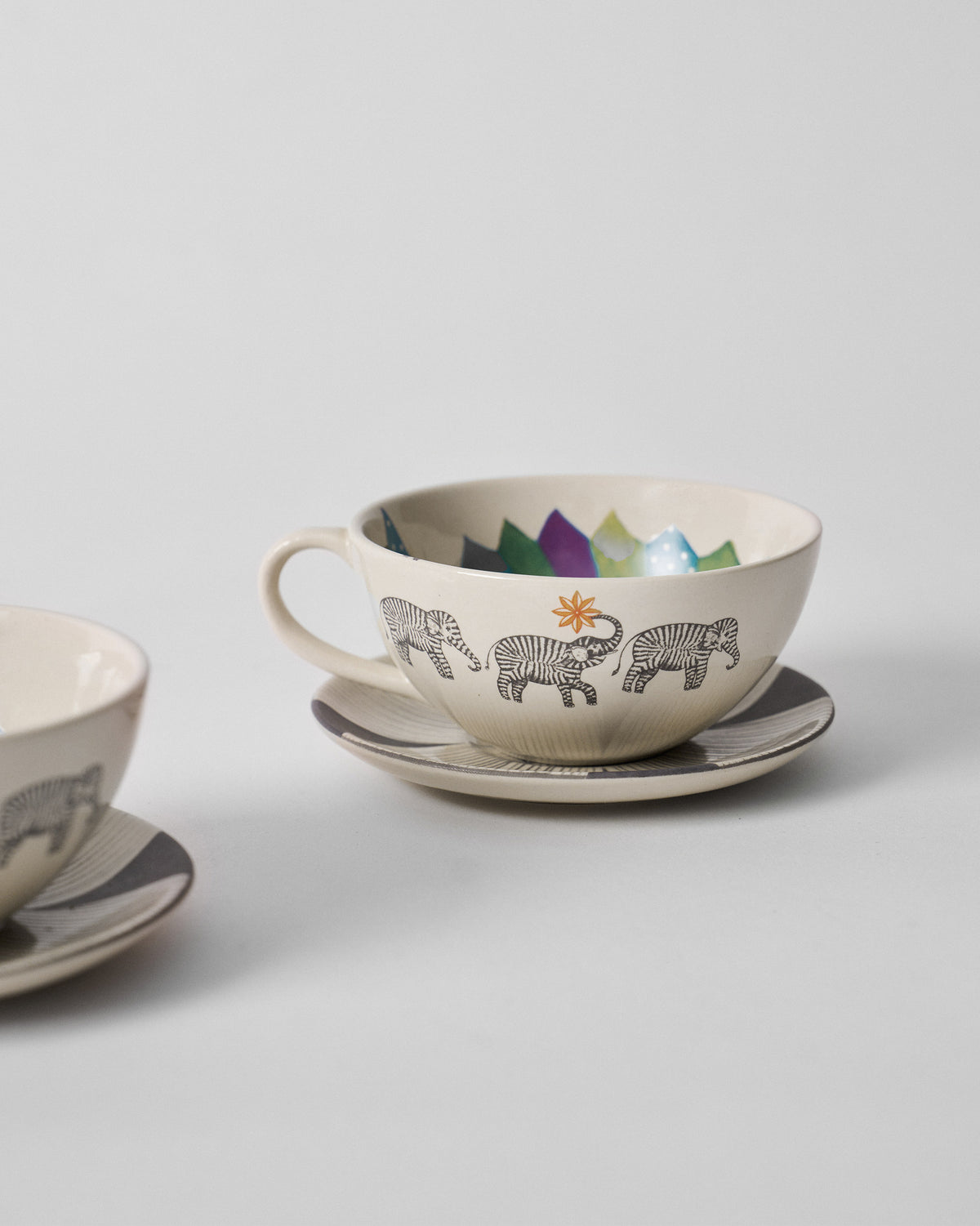 Palm Bloom coffee cup with striped elephants and a colorful interior rim on its saucer.