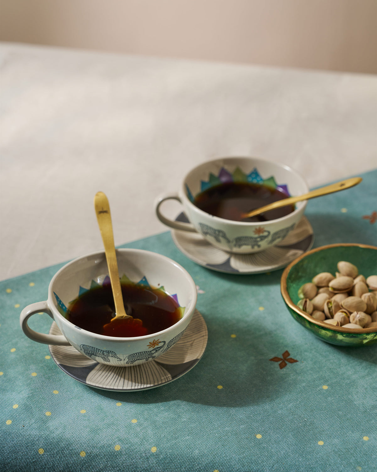 Palm Bloom coffee cups filled with coffee and gold spoons on matching saucers.