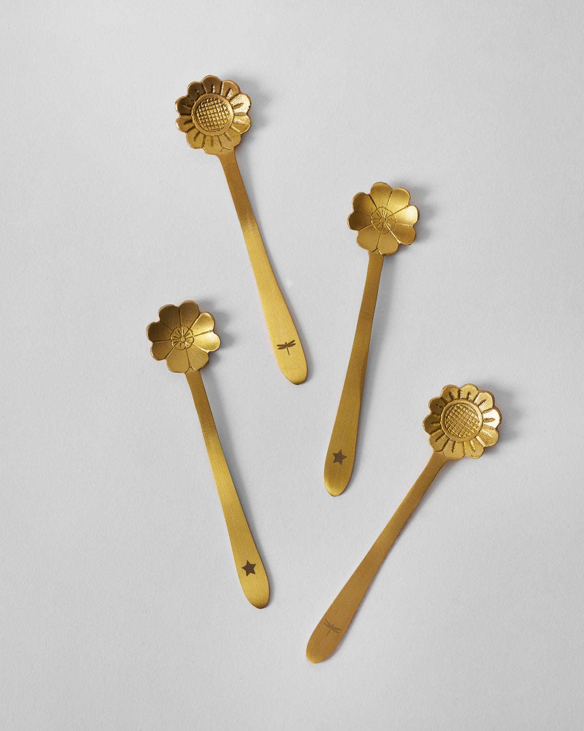 Four matte gold Phool coffee spoons with alternating flower head designs.