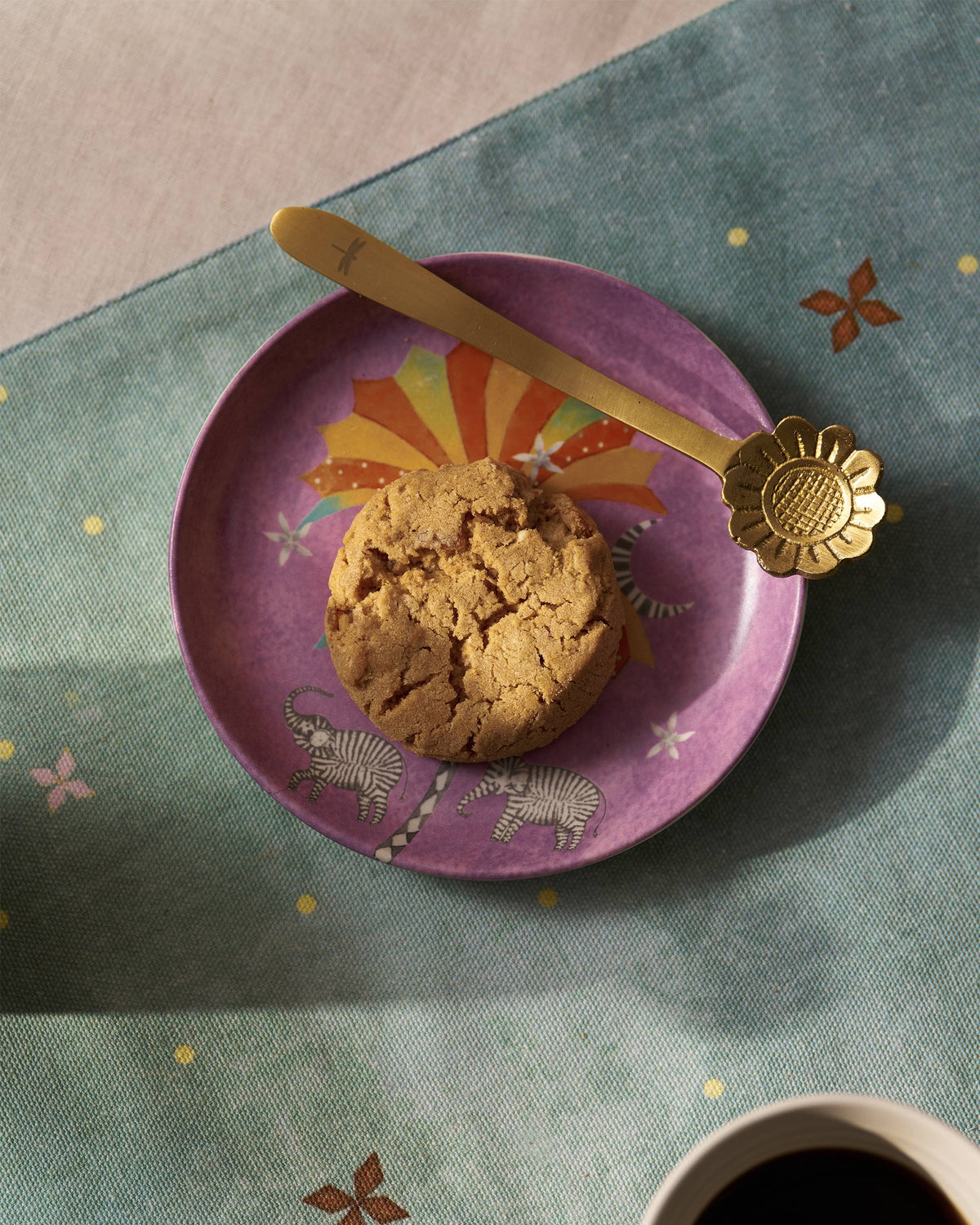 Gold Phool coffee spoon with a sunflower head resting on a purple plate.