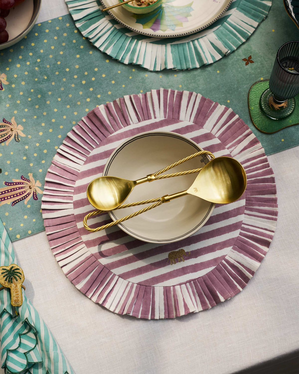 Tusk gold serving spoons crossed in a bowl on a placemat.