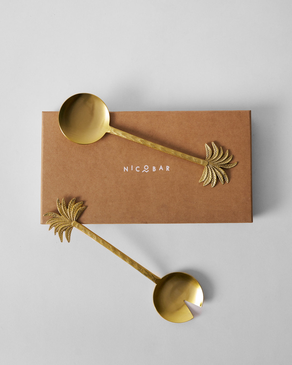Palm Bloom salad servers resting across a brown Nicobar box.