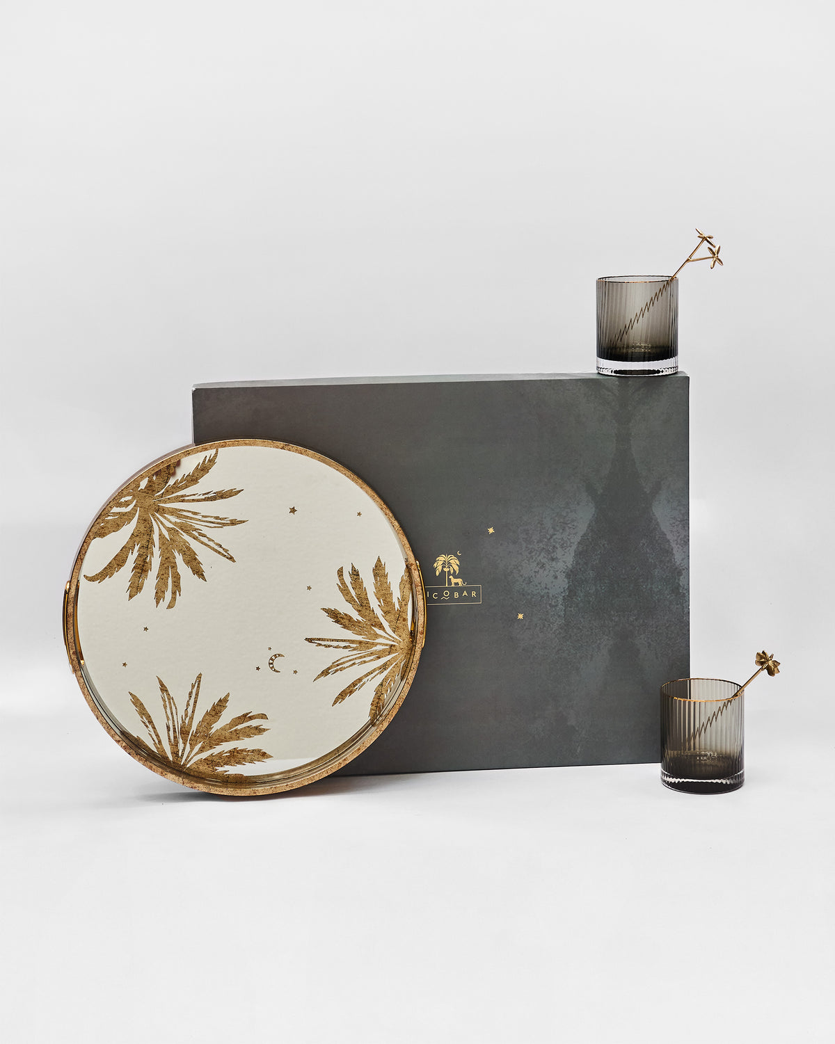 Gilded Palm gift set with palm-print tray, fluted glasses and gold stirrers by its box.