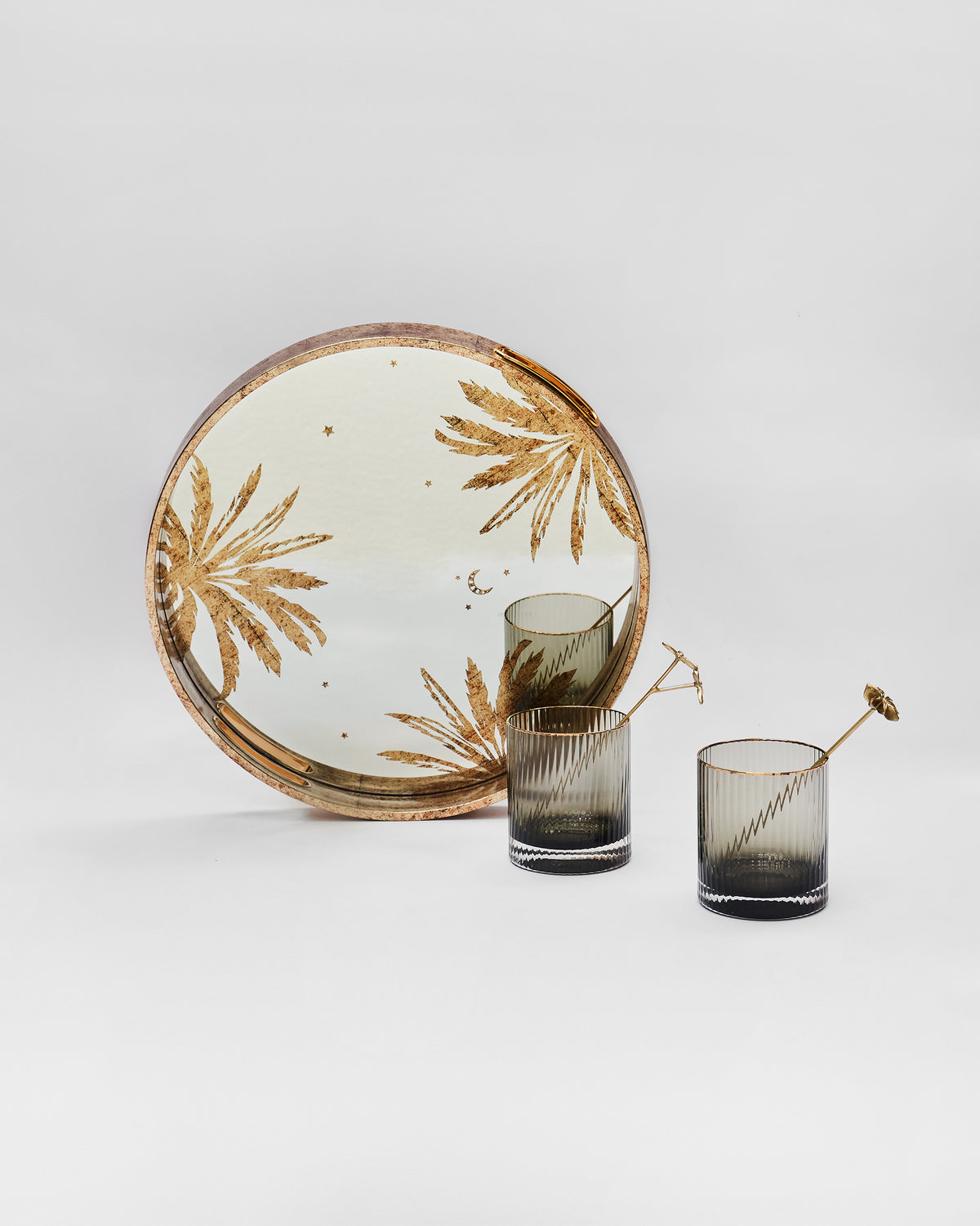 Gilded Palm tray with gold palm motifs behind two fluted glasses and stirrers.