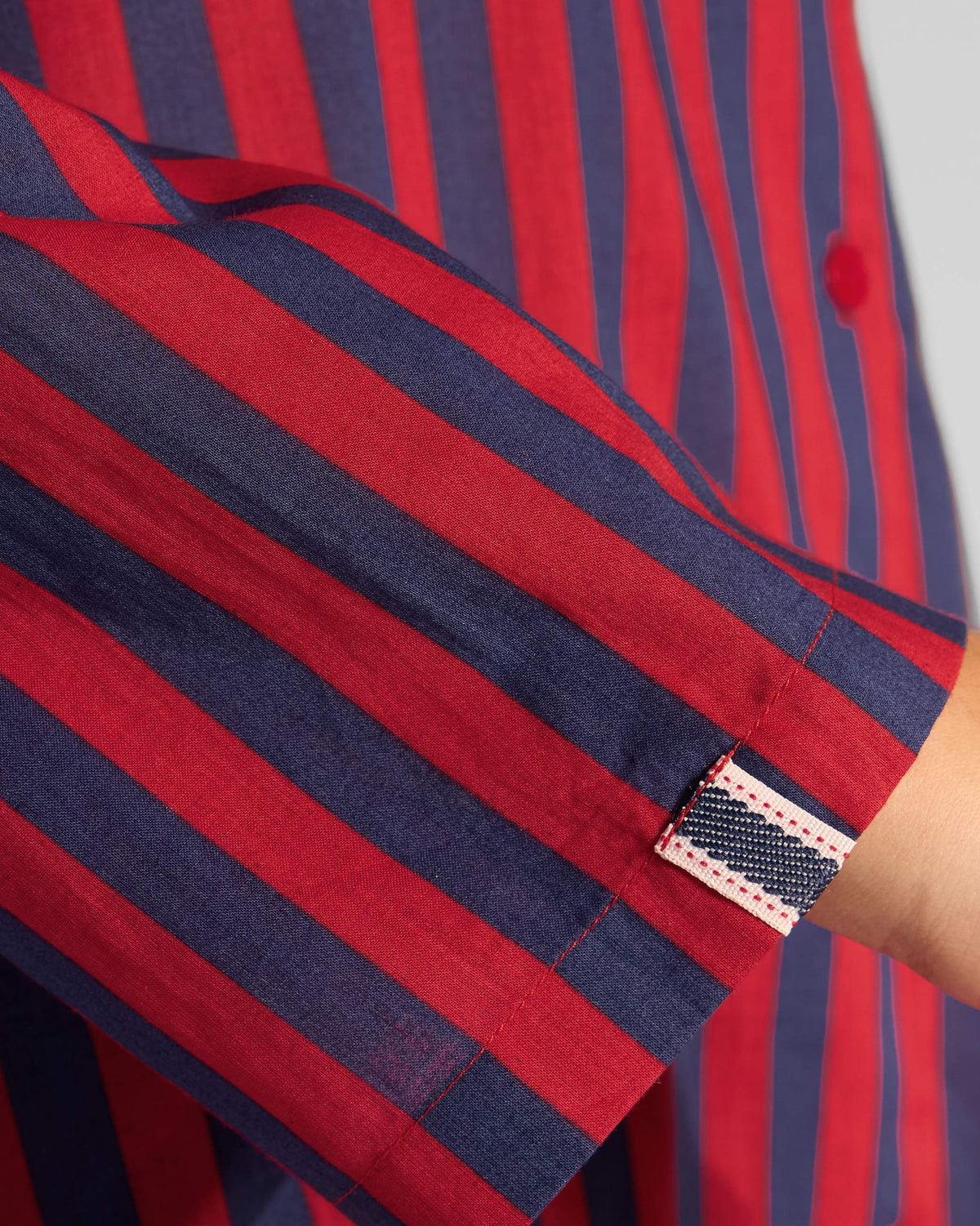 Close-up of a sleeve tab on a red and navy striped Nimar long shirt.