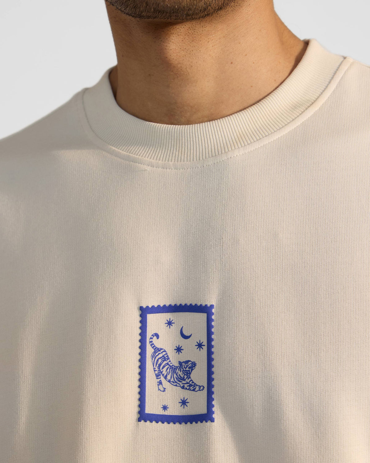 Close-up of the blue leaping tiger stamp print on an ivory crew-neck t-shirt.