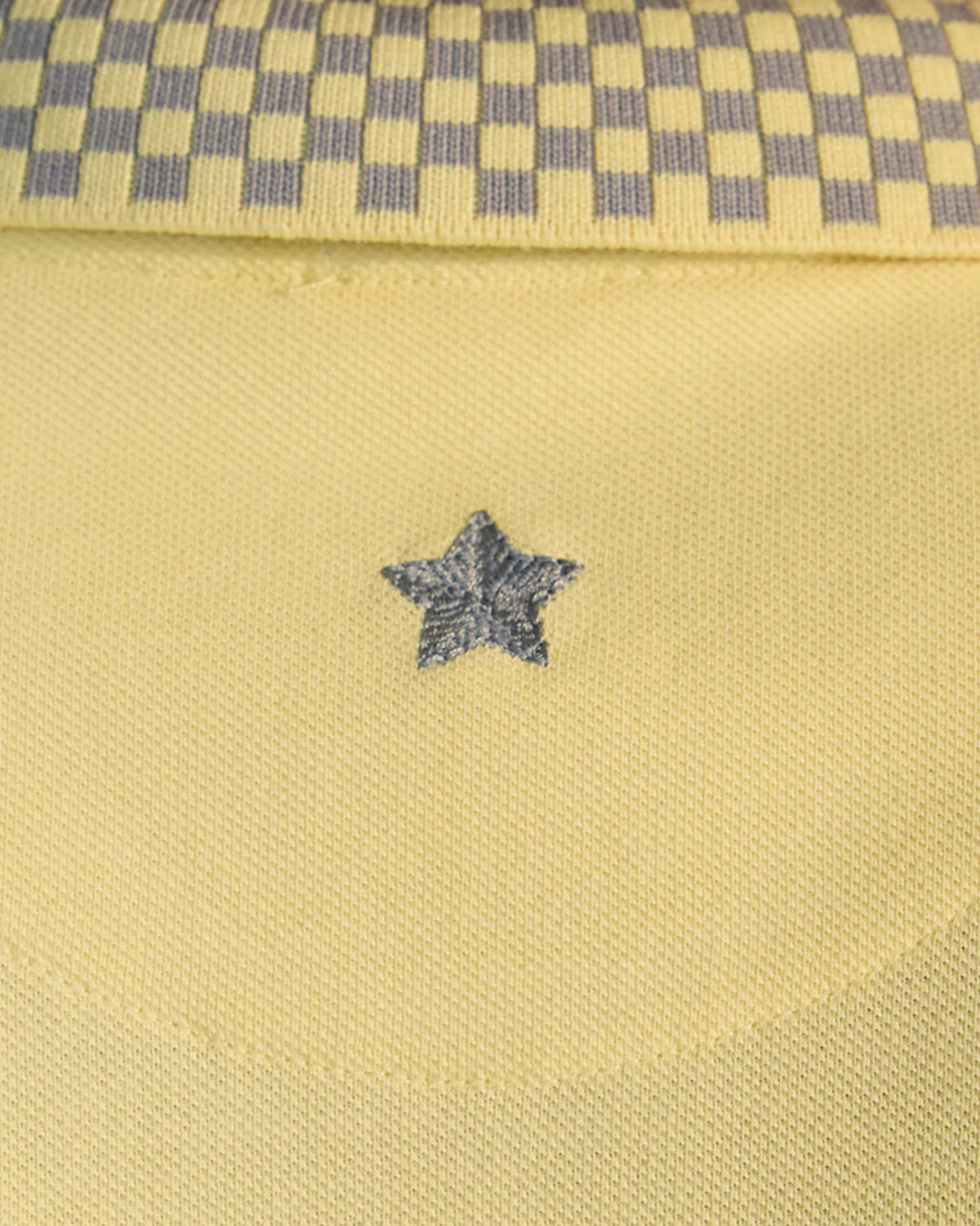 Close-up of a grey star embroidery below the checkered collar of a light yellow polo.