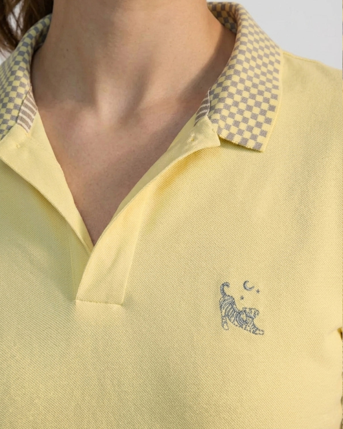 Close-up of a light yellow polo showing a checkered collar and tiger chest embroidery.
