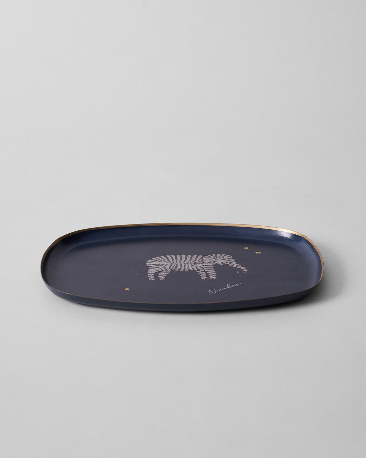 Shallow navy Tusk trinket tray with a gold rim and striped elephant motif.