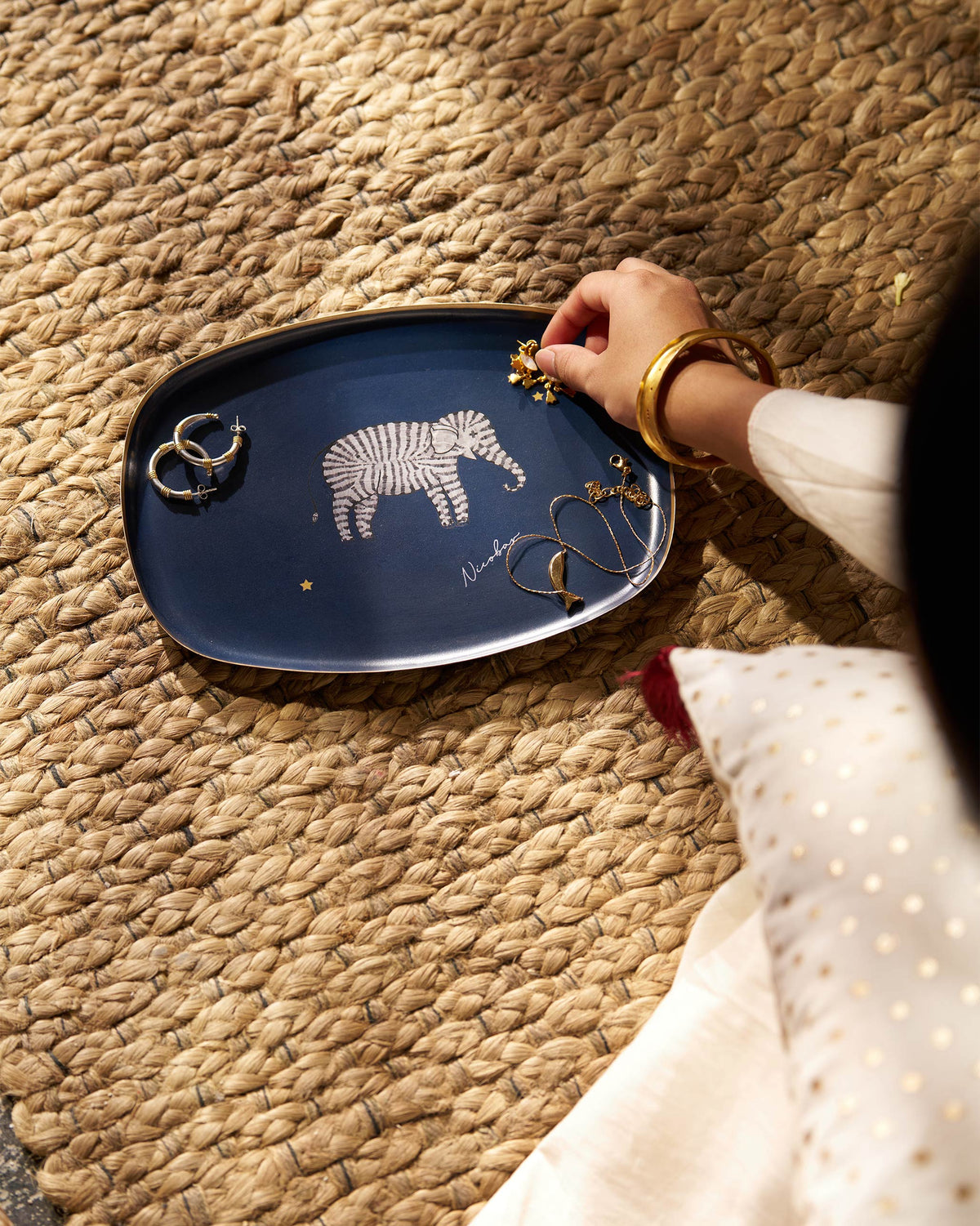 Navy Tusk trinket tray holding earrings and a necklace on a woven rug.