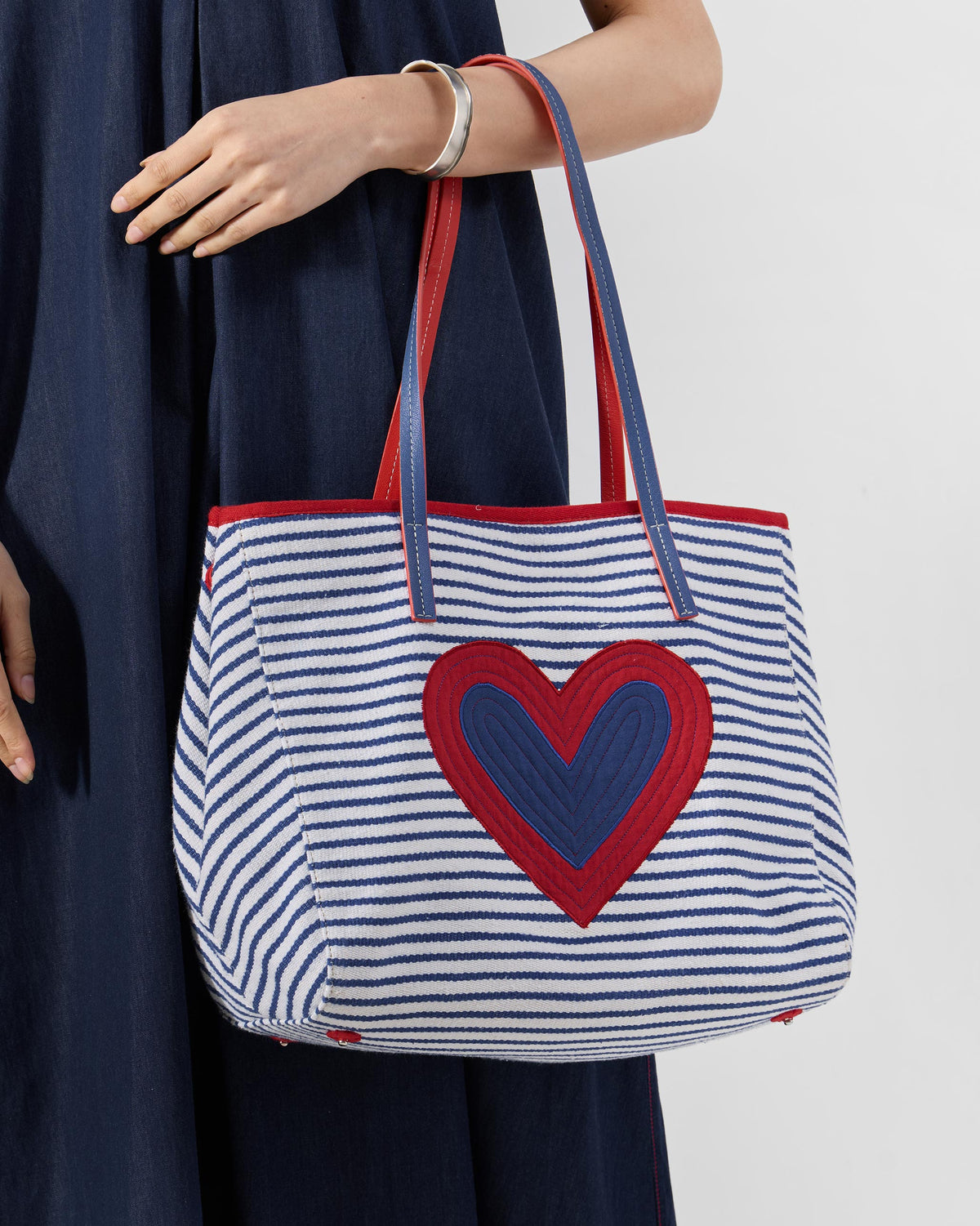 Blue and white striped Kira Bag with a red and blue heart, carried on the arm.