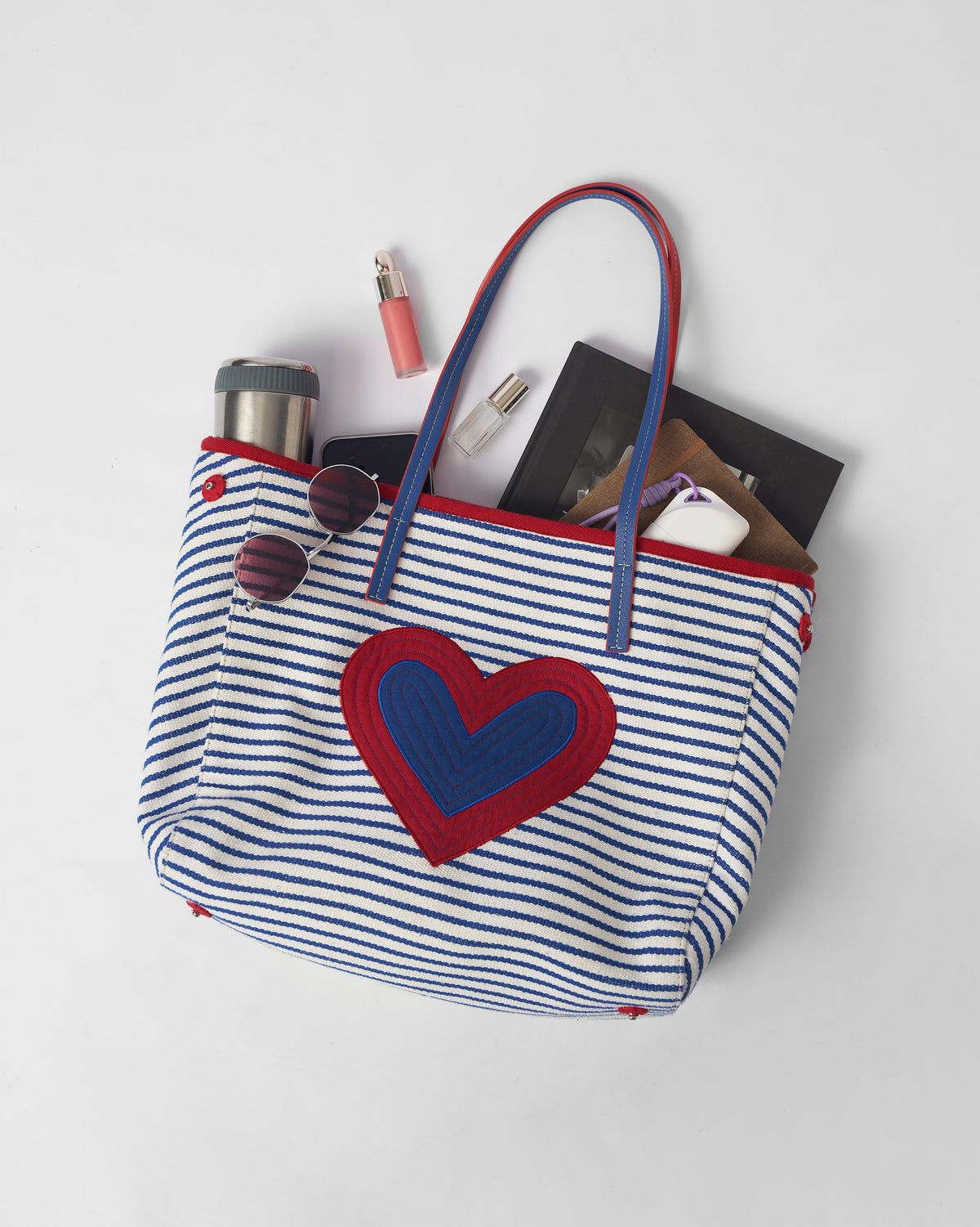 Open blue and white Kira Bag packed with a bottle, notebook, and essentials.